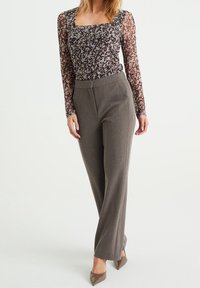 Långärmad topp med blommönster i nyanser av lila och kräm, tillsammans med högmidjade grå byxor och bruna spetsiga klackar.