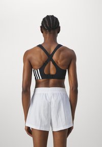 Svart sportsbh med kryssede stropper og hvite striper; kombinert med hvite shorts med elastisk midje; glatt tekstur og atletisk design.
