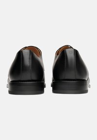 Schwarze Lederschuhe mit glatter Textur, abgerundeten Absätzen und minimalen Nähdetails. Das Innere verfügt über eine kontrastierende hellbraune Innenausstattung.