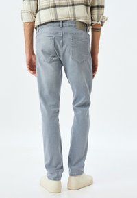 Jeans de color azul claro con un corte ajustado, que presentan bolsillos traseros cosidos y una etiqueta de cuero con la marca en la cinturilla. Textura de denim suave.