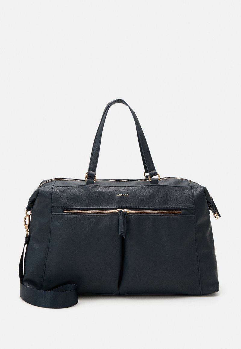Sac de voyage en cuir bleu marine avec deux poignées supérieures, une bandoulière amovible et des garnitures en métal doré. Comprend deux poches zippées à l'avant.