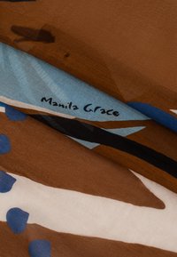 Tissu à motifs marron et bleu avec une texture douce, mettant en avant une étiquette "Manila Grace" bien visible. Les nuances se mélangent harmonieusement en formes abstraites.