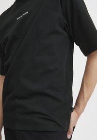 Svart bomull T-skjorte med korte ermer, med en liten hvit logo tekst "Casual" på brystet. Litt avslappet passform og glatt tekstur.