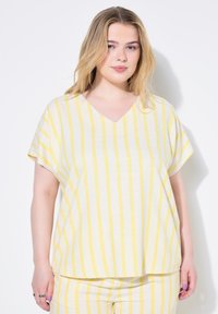 Top à col en V, à manches courtes, en tissu léger. Présente des rayures horizontales blanches et jaunes. Coupe ample avec un ourlet droit.