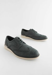 Zapatos de cuero gris oscuro con detalles perforados, diseño con cordones y suela clara en contraste. Punta redondeada, textura suave y construcción robusta.