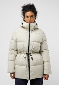 Lichtbeige pufferjack met een getailleerde taille, zwarte rits en verstelbare capuchon. Heeft een gladde, glanzende stof en brede mouwen.