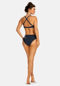 Granatowy zestaw bikini z krzyżującymi się ramiączkami, wysokim stanem i teksturowanym materiałem z małymi świecidełkami. Widok z tyłu.