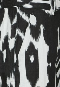 Černobílá látka se vzorem s výrazným designem ikat. Textura je hladká, s viditelnými sklady a detailním pásem.