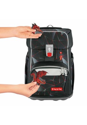 Sac à dos noir à motif géométrique avec des accents rouges et une fermeture éclair à l'avant. Un porte-clés en forme de dragon rouge est accroché au sac.