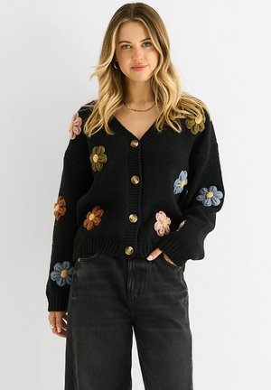 Black knitted cardigan with floral appliqués in various colors and gold buttons, featuring a V-neck and ribbed cuffs.