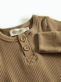 Brun ribbad långärmad skjorta med rund halsringning, två knappar och en liten broderad triangel. Taggen säger "MarMar Copenhagen."