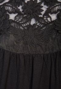 Svart klänning med en blomster spets överdel med intrikata broderimönster, en slät midja och en fladdrande, samlad kjol.