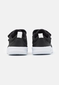 Zapatillas negras con parte superior de malla y sintético, suela de goma blanca. Cuenta con una lengüeta y cierre de correa. La vista trasera muestra materiales en contraste.