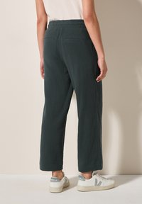 Relaxed-fit, dark green trousers made of textured fabric, featuring an elastic waist and two back pockets. Paired with white sneakers.