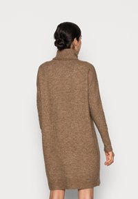 Översized brun stickad klänning med hög krage, långa ärmar och ribbade mudd och fåll, tillverkad av ett mjukt, texturerat tyg.