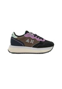 Sneaker in suede nero e materiale sintetico marrone, con accenti viola e teal, lacci testurizzati e una robusta suola intermedia bianca.