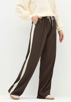 Pantaloni marroni con strisce laterali crema, caratterizzati da una vestibilità relaxed, cintura elasticizzata e tasche, abbinati a un maglione crema testurizzato.