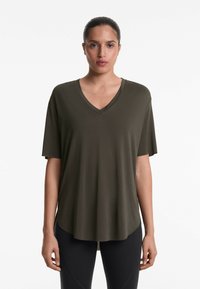 Oliven grøn V-hals T-shirt med korte ærmer, blødt stof, buet kant og afslappet pasform, båret med sorte leggings.