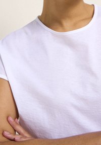 T-shirt bianca a girocollo con maniche a cappuccio, realizzata in morbido cotone, che presenta una texture liscia e un design minimale, senza motivi visibili o dettagli.