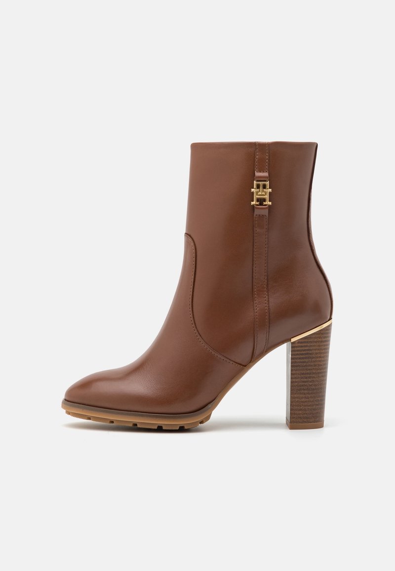 Bottes courtes en cuir marron avec un bout pointu, des accents métalliques dorés et un talon en bois empilé. Texture lisse avec un design élégant.