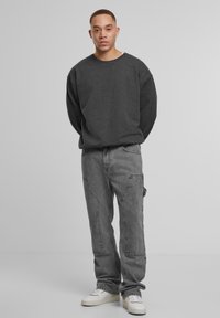 Grauer übergroßer Sweatshirt, graue Cargo-Hosen mit Patchdetails und weiße Sneakers. Das Outfit bietet eine lockere Passform und eine weiche Textur.