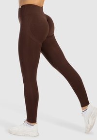 Leggings marroni a vita alta realizzati in tessuto elasticizzato, con un design sagomato e abbinati a scarpe da ginnastica bianche.