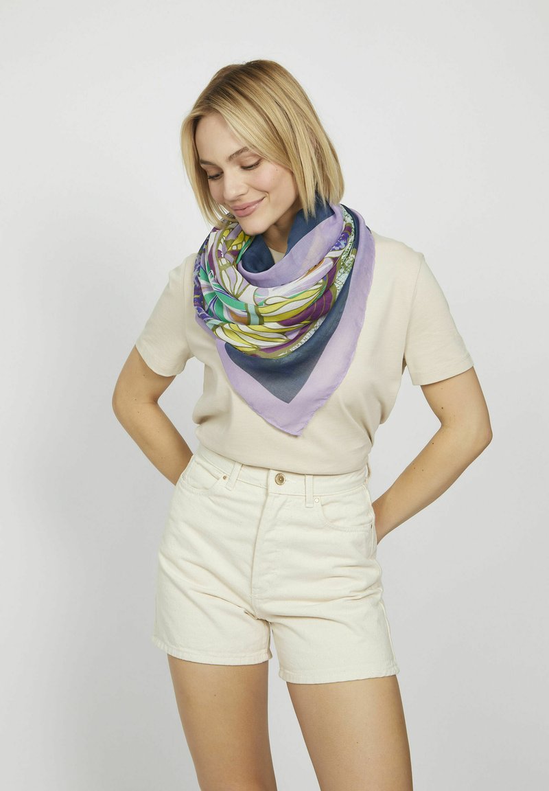 Écharpe en soie multicolore de forme triangulaire, ornée de motifs floraux dans des teintes de vert, violet et bleu marine, drapée autour du cou.