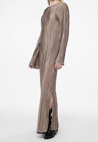 Robe longue plissée d'une couleur beige atténuée, avec des fentes et des manches longues. Fabriquée dans un tissu léger et texturé.