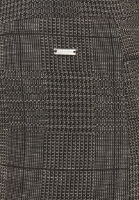 Black and white woven fabric with a detailed geometric pattern and a small silver tag labeled "TASCANA" attached.