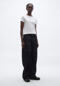 Fehér pamut rövid ujjú póló kis hímzett díszítéssel, sötétkék, széles szárú farmernadrággal, látható varrással párosítva.