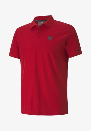 Rotes Polohemd mit kurzen Ärmeln, Kragen und drei Knöpfen, mit einem kleinen dunklen Emblem auf der linken Brust und einem schmalen schwarzen Streifen an den Ärmeln.