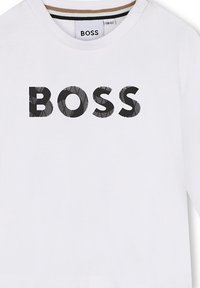 T-shirt bianco a maniche lunghe con un prominente logo nero "BOSS" caratterizzato da un motivo testurizzato. Include un collo a giro e bottoni sulle spalle.
