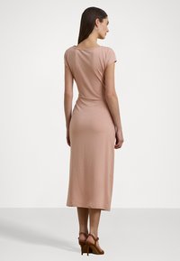 Abito midi aderente in rosa pallido, con maniche a soffietto, scollatura rotonda e superficie liscia, abbinato a tacchi marroni con cinturini.