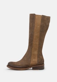 Botas altas de ante marrón con diseño bicolor; presentan una puntera ligeramente redondeada y un tacón apilado, con una parte superior texturizada y paneles en contraste.