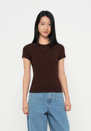 Brun fittet t-skjorte med korte ermer, rund hals og en liten logo detalj i midten. Brukt med lyseblå, løstsittende jeans.