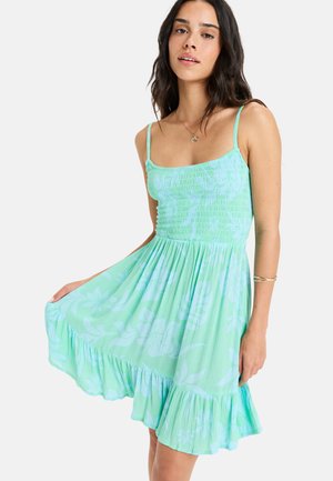 Mint green flared dress with thin straps, smocked bodice, and a tiered ruffled hem featuring a subtle floral pattern. Soft textured fabric.