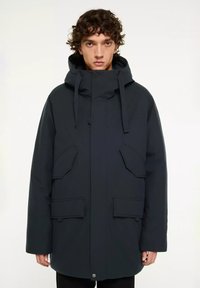 Donkerblauwe parka met capuchon, voorzien van een ritssluiting en knoopsluiting, twee schuin geplaatste zakken aan de voorkant en een gestructureerde stof.