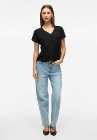 Blusa nera a maniche corte con scollo a V e dettagli arricciati, abbinata a jeans azzurri chiari a vita alta e ghette color bordeaux.