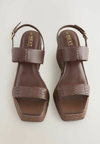 Brown wedge sandals with two wide straps and an ankle buckle, featuring a textured cork-like sole and a sleek design.