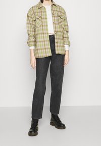 Green and beige checkered flannel shirt with two front pockets, paired with dark gray straight-leg jeans and black lace-up boots.