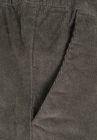 Grå kordfärgad tyg med vertikal ribbad struktur. Elastiskt midjeband med sidofickor. Närbild som betonar tygdetaljer.