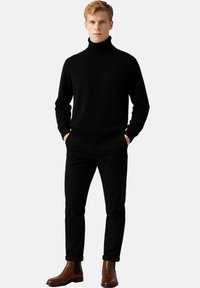 Schwarzer Rollkragenpullover mit Rippdetails, kombiniert mit schwarzen Slim-Fit-Hosen und braunen Stiefeletten. Schlichtes, elegantes Design.