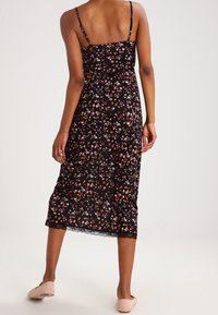 Schwarzes Blumenkleid mit dünnen Trägern, das eine taillierte Oberkörperpartie und einen fließenden Rock aufweist, am Saum mit zarter Spitze verziert.