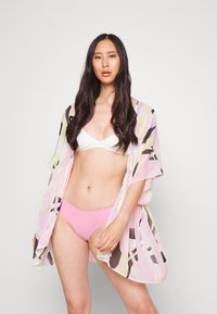 Kimono transparente em rosa, amarelo e padrão geométrico em preto, usado sobre um top de bikini branco e uma parte baixa de bikini rosa. Design fluído com mangas curtas.