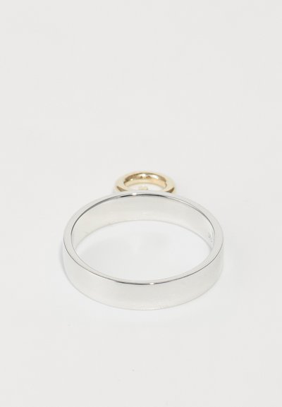Silber- und Goldring mit einem glatten, abgerundeten Band und einem kreisförmigen goldenen Akzent oben. Das Design ist minimalistisch und modern.