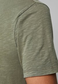 Oliven grøn bomulds t-shirt med korte ærmer, der har et blødt, tekstureret stof og kontrastsyning langs kanterne.
