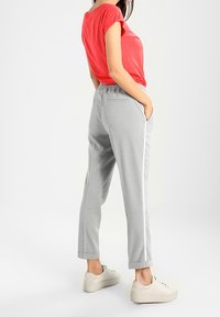 Pantalon gris fuselé avec des rayures latérales et une taille élastique, associé à un haut rouge à manches courtes et des baskets crème. Look simple et décontracté.