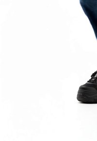 Musta platvorm-treeningkinga inimese jalal, osaliselt nähtav, ühevärvilise valge tausta vastu.