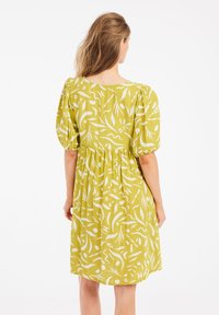 Kurzes grünes Kleid mit weißen abstrakten Mustern, rundem Ausschnitt und geraffter Taille. Aus leichtem Stoff, knielang.