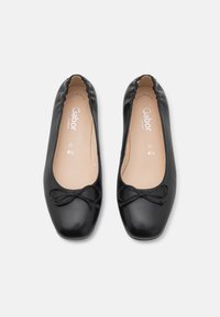 Une paire de ballerines en cuir noir avec de petits noeuds, des bords élastiques et des semelles intérieures beiges marquées "Gabor Comfort" et taille 4½ G.
